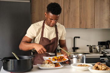Fototapeta na wymiar Young black man serving plantain on tomato sauce fried chicken mince and rice plate in a kitchen.