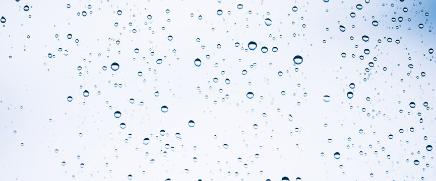 Minimal light backdrop with rain droplets on white glass. Light wet window with rainy drops closeup in blue light. Blurry minimalist monochrome background of window glass with raindrops close up.
