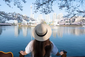 Selbstklebende Fototapete Seoel Asian lady travel in cherry blossom park in Seoul city,South Korea with Sakura flower and Lotte World Tower and Seokchon Lake background.