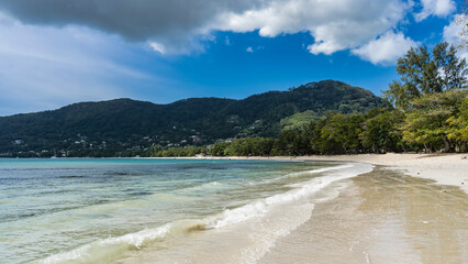 The waves of the turquoise ocean roll onto the beach. Wet sand glistens . Green vegetation on the...