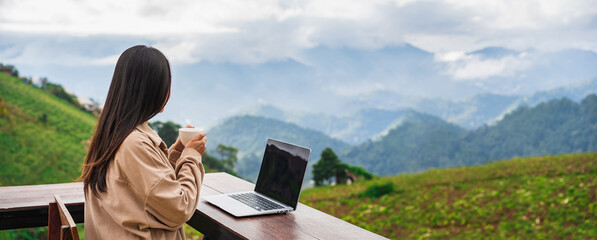 Young woman freelancer traveler working online using laptop and enjoying the beautiful nature landscape with mountain view - 590399296