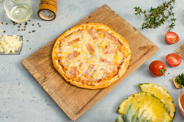 Top view shot of delicious tasty juicy of Hawaiian traditional Italian crust thin crispy ham and pineapple pizza placed on wooden cutting board with ingredients sliced tomatoes, ketchup and salt