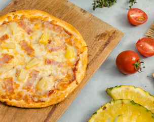 Top view shot of delicious tasty juicy of Hawaiian traditional Italian crust thin crispy ham and pineapple pizza placed on wooden cutting board with ingredients sliced tomatoes, ketchup and salt