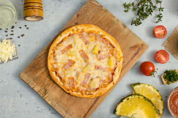 Top view shot of delicious tasty juicy of Hawaiian traditional Italian crust thin crispy ham and pineapple pizza placed on wooden cutting board with ingredients sliced tomatoes, ketchup and salt