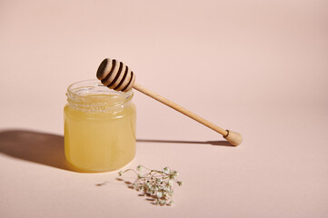 Still life with a wooden dripper on a jar with organic honey and dried bouquet of meadow flowers, isolated on pink pastel background.