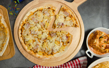 Top view shot of various kinds of delicious tasty juicy cheesy pizza placed on wooden board on party table around with other fast food  for eating dinner together.