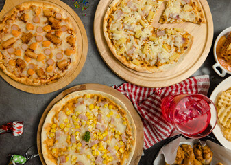 Top view shot of various kinds of delicious tasty juicy cheesy pizza placed on wooden board on party table around with other fast food  for eating dinner together.