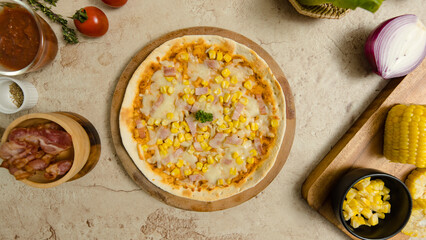 Top view closeup shot of delicious tasty juicy thin crispy cheesy corn and ham Italian pizza placed on wooden board on party table around with other ingredients, sauce, olive oil, bacon and tomatoes