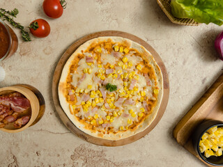 Top view closeup shot of delicious tasty juicy thin crispy cheesy corn and ham Italian pizza placed on wooden board on party table around with other ingredients, sauce, olive oil, bacon and tomatoes