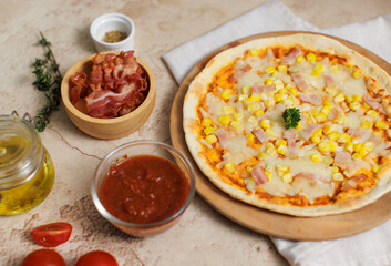 Top view closeup shot of delicious tasty juicy thin crispy cheesy corn and ham Italian pizza placed on wooden board on party table around with other ingredients, sauce, olive oil, bacon and tomatoes