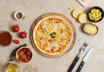 Top view closeup shot of delicious tasty juicy thin crispy cheesy corn and ham Italian pizza placed on wooden board on party table around with other ingredients, sauce, olive oil, bacon and tomatoes