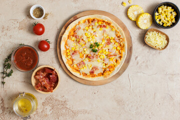 Top view closeup shot of delicious tasty juicy thin crispy cheesy corn and ham Italian pizza placed on wooden board on party table around with other ingredients, sauce, olive oil, bacon and tomatoes
