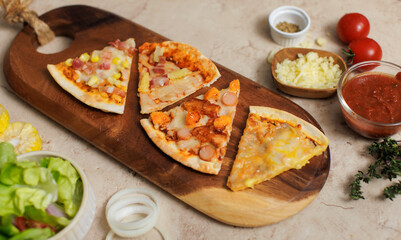Top view shot various kinds of delicious tasty juicy thin crispy cheesy sliced Italian pizza placed on wooden cutting board on party table around with other ingredients, sauce, corn, cheese, tomatoes