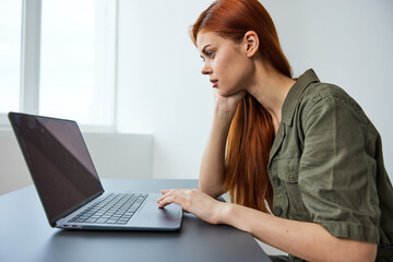 woman interested in work sits at a table and works in a laptop in a bright room