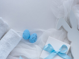 Obraz na płótnie Canvas Wellness Easter concept. Set towels in white colors, blue eggs, gift box, bunny and copy space. White Easter card. Rolled towels in spa salon. Hygiene and spa, relaxation as a gift for holidays
