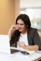 Smiling confident Indian woman using laptop computer having video call in office. Successful asian freelancer working online sitting at workplace. Modern technology, video conference concept