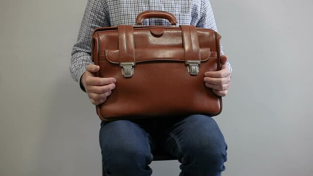 A man sits nervously in an armchair and holds a brown leather briefcase on his knees. The businessman gets up and leaves without waiting.