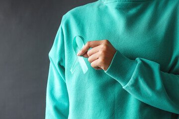 Woman hands wearing teal t-shirt holding teal awareness ribbon. Support cancer survivor. Ovarian Cancer month, cervical cancer day. 