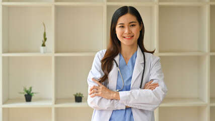 Positive female doctor in white coat with stethoscope standing with arms crossed and smiling at camera. Healthcare and medical