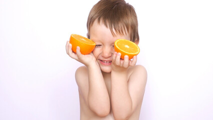 A confused little boy laughs holding two halves of an orange in his hands