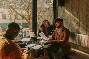 White good looking male person reading a document while working remotely with his multiracial colleagues. His female ginger coworker is having a phone call