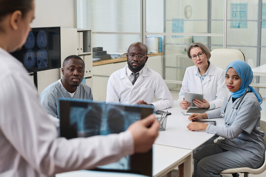 Doctor showing x-ray image of lungs to his colleagues and discussing disease with them during teamwork in office