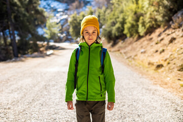 boy with a backpack in the forest. The child is standing in the middle of the road in the forest.