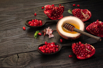 Natural liquid honey is poured into a coconut cut in half, the coconut is located on a black, old, wooden table, decorated with pieces of ripe, red, juicy, pomegranate, green mint leaves, sakura flowe