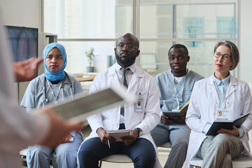 Fototapeta premium Group of serious doctors listening to speaker nd making notes during medical seminar in office