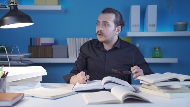 The young man who reads books, learns science and does research is in a state of astonishment.
Young man with glasses is sitting in his study, reading a book, doing research and being surprised by wha