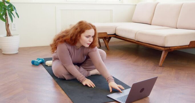 serious ambitious plaump red head girl concentrated on repeting fitness movement, loking at the screen of laptop, following advise, slow motion. online workout course to lose weight