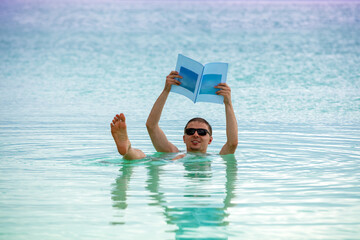 A man swims on his back in the Dead Sea with a magazine in his hands