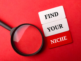 Wooden board and magnifying glass with text FIND YOUR NICHE on a red background.