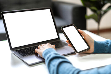 Woman working with smartphone and modern laptop computer blank white desktop screen for...