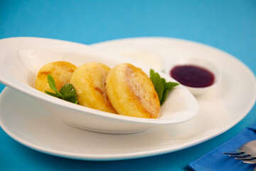 Round cottage cheese pancakes in a white plate on a blue background. Food breakfast. Healthy food. Sour cream sauce and mint. Top view closeup. Dessert meal. Curd cheese pancake ricotta fritters.