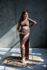 A happy young pregnant woman in a brown delicate suit is posing and stroking her belly. Pregnant pregnant woman. Happy pregnancy