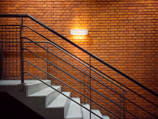 Side view of the stairs near the red brick wall. A light fixture on a brick wall illuminates the stairs
