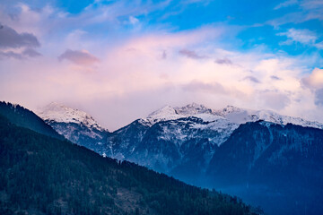 Obraz na płótnie Canvas monsoon clouds moving over snow covered himalaya mountains with the blue orange sunset sunrise light over kullu manali valley