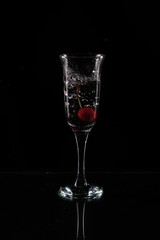A glass of water and a cherry falling into the water
