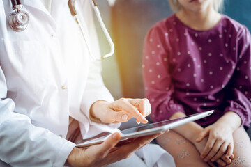 Doctor woman and kid patient at home. The pediatrician uses a tablet computer, close up. Medicine, healthcare concepts