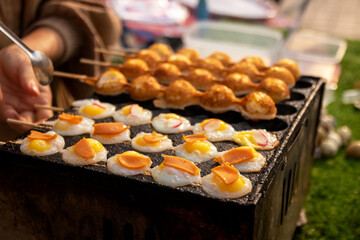 Fried Quail eggs in bamboo skewers on pothole pan. Drop each egg in a small ramekin gently slide it into the hot oil. Serve warm with salt and ground pepper. Thai appetizer at street food market.
