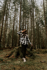 Stylish hipster girl in a hat wrapped in a checkered plaid posing in the base of a pine forest.Travel concept