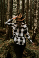 Stylish hipster girl in a hat wrapped in a checkered plaid posing in the base of a pine forest.Travel concept