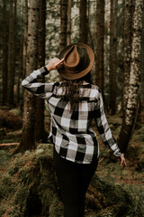 Stylish hipster girl in a hat wrapped in a checkered plaid posing in the base of a pine forest.Travel concept