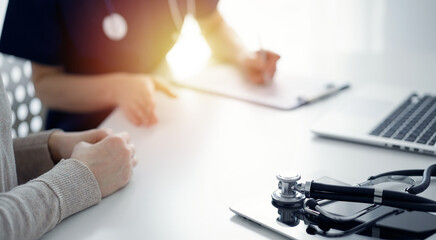 Stethoscope lying on the tablet computer in front of a doctor and patient at the background. Medicine, healthcare concept