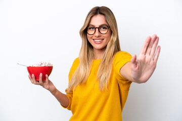 Young Uruguayan woman holding a bowl of cereals isolated on white background saluting with hand with happy expression