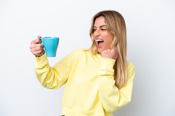 Young Uruguayan woman holding cup of coffee isolated on white background celebrating a victory