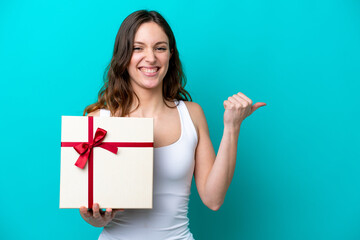 Young caucasian woman holding a gift isolated on blue background pointing to the side to present a product