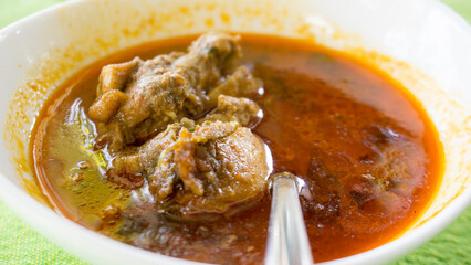 Close up of a bowl of Sri Lankan chicken curry with a spoon on a table