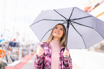 Young pretty Romanian woman holding an umbrella at outdoors celebrating a victory